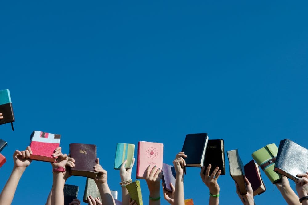 Colorful books being held up against a bright blue sky at AEGA Ministries International, Inc., emphasizing spiritual growth, faith, and community outreach.