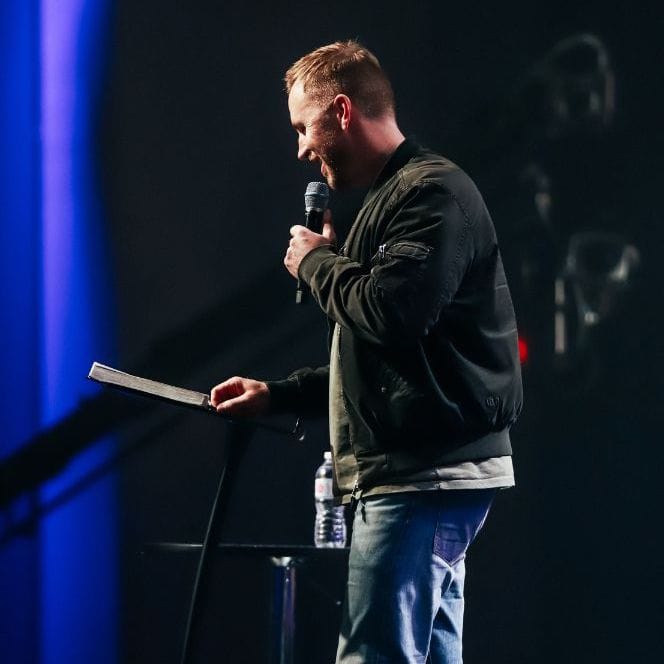 Aega Ministries International, Inc., religious speaker delivering a sermon on stage with a microphone and open Bible, engaging audiences in faith-based teachings, Christian ministry, and spiritual growth.