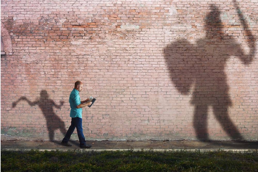 Shadow of a man reading a book projected on a brick wall, symbolizing faith, spiritual growth, and divine guidance; represents AEGA Ministries International, Inc., emphasizing spiritual outreach and religious teachings.