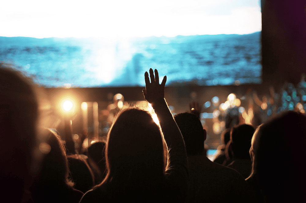 Vibrant scene of a religious gathering at AEGA Ministries International, Inc., with attendees raising hands in worship against a backdrop of a sea and sunset, emphasizing faith and community.